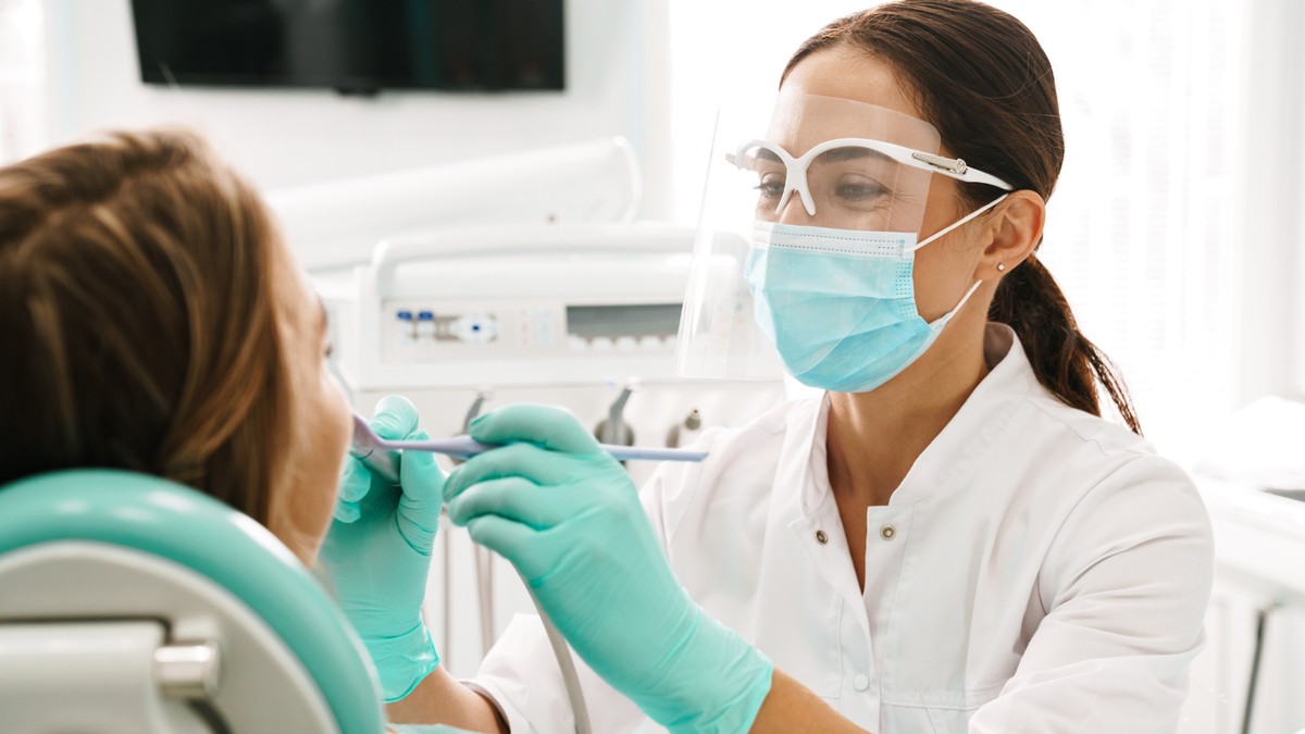 Dentystka ubrana w maseczkę dokonuje przeglądu zębów pacjentce na fotelu dentystycznym
