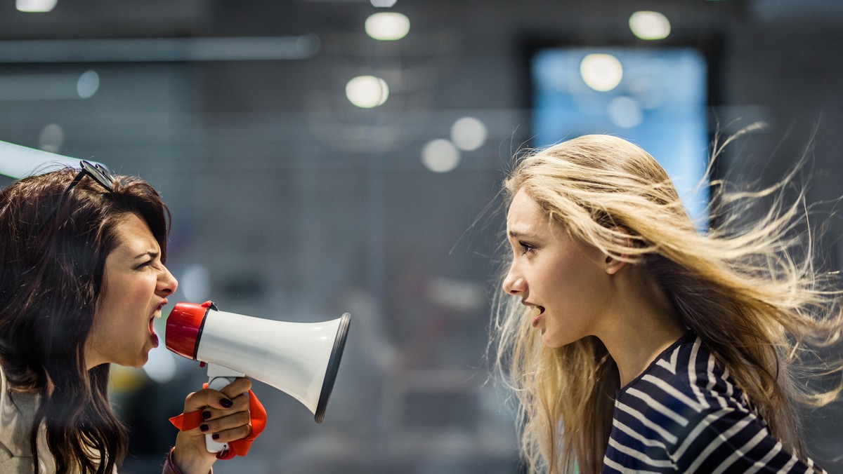 Profile view of angry female manager yelling at her colleague through megaphone.