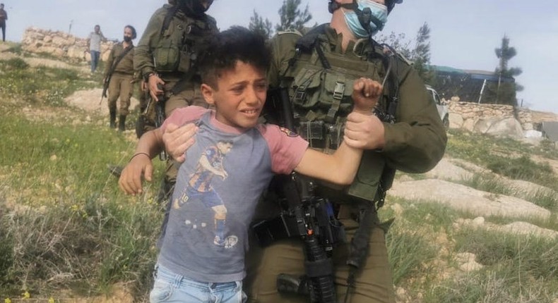 A Palestinian child is carried by an Israeli soldier to a vehicle on the outskirts of Havat Maon in the West Bank on March 10, 2021.
