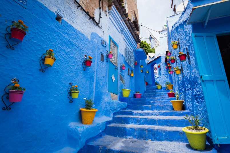 Chefchaouen „Niebieskie Miasto” jak zwykło się określać Chefchaouen położone jest w północno-zachodniej części Maroka, pośród skalistego pasma górskiego Rif, określającego fizyczną granicę między Europą i Afryką. To świetne miejsce na wędrowanie i popijanie miętowej herbaty. Jest tu bardzo spokojnie, ale miejsce to potrafi też oszołomić. Niemal wszystkie budynki są pomalowane żywym błękitem, ale zabudowa wcale nie jest przez to monotonna – można tu chyba zobaczyć każdy odcień tego koloru: błękit, indygo, kobalt, lazur, cyjan, szafir… nieskończona gama odcieni sprawia, że miasto wydaje się wręcz tryskać kolorami, a marokańskie łuki tylko podkreślają wyjątkowość tej architektury. Trudno porównać Chefchaouen z jakimkolwiek innym miastem na świecie. Zabudowania wkomponowane pomiędzy strome zbocza, wiszące tuż nad urwiskiem przypominać mogą nieco Santorini – tam jednak błękit wyłania się z wód widocznych na horyzoncie, tutaj błękitne są niemal wszystkie budynki, a zamiast morza dookoła roztaczają się góry. Pobyt w tym miejscu nie może się wręcz obejść bez górskiej wycieczki. Warto wybrać się zwłaszcza nad Cascades d'Akchour, parę wodospadów (górna kaskada ma około stu metrów, niższa około dwudziestu) położoną w górach, około 45 minut od miasta. Malownicza trasa prowadzi między innymi przez naturalny most zwany Mostem Boga, a na miejscu można popływać w otoczonym bujną roślinnością, krystalicznie czystym, turkusowym basenie. Źródło: r.pl/maroko >>