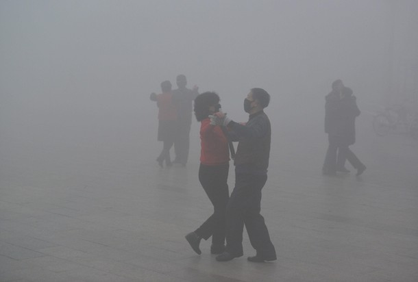 People wearing masks dance at a square among heavy smog during a polluted day in Fuyang