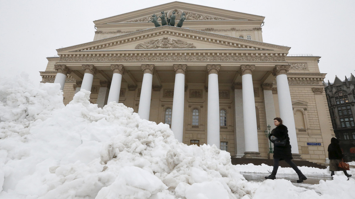 People walk near the Bolshoi Theatre, with heaps of snow seen in the foreground, in central Moscow, Russia