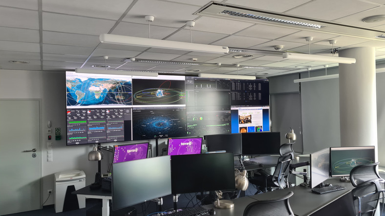 Sala operacyjna w Departamencie Bezpieczeństwa Kosmicznego Polskiej Agencji Kosmicznej. Ekrany na ścianie wyświetlają różne informacje z systemów informatycznych, za pomocą których monitorowana jest sytuacja na orbicie.