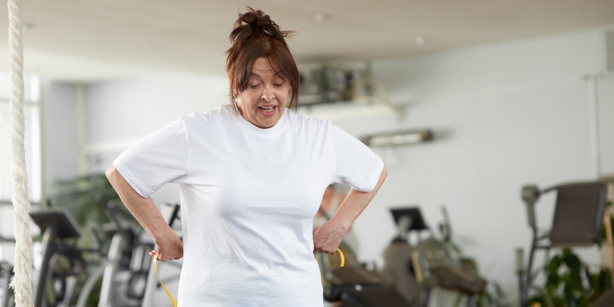 Elderly woman measuring her waist at gym.