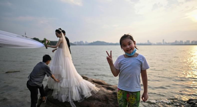 A girl gestures while a couple poses for a wedding photographer next to East Lake in Wuhan