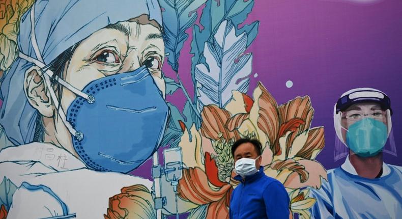 A man wearing a face mask walks past a mural at Leishenshan Hospital in Wuhan in April