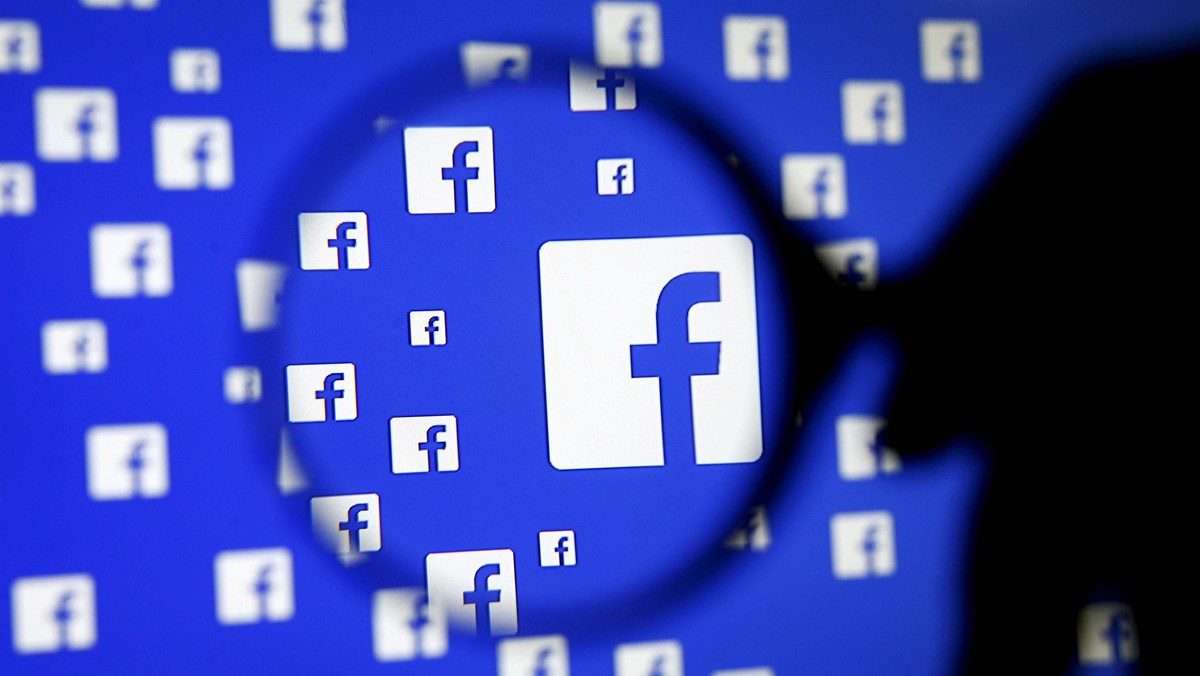 A man poses with a magnifier in front of a Facebook logo on display in this illustration taken in Sa