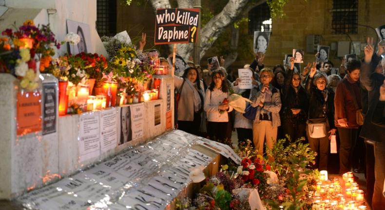 People hold portraits as they stand beside lighted candles placed in memory of murdered journalist Daphne Caruana Galizia on the sixth month anniversary of her death at a makeshift memorial outside the law courts in Valletta, Malta on April 16, 2018