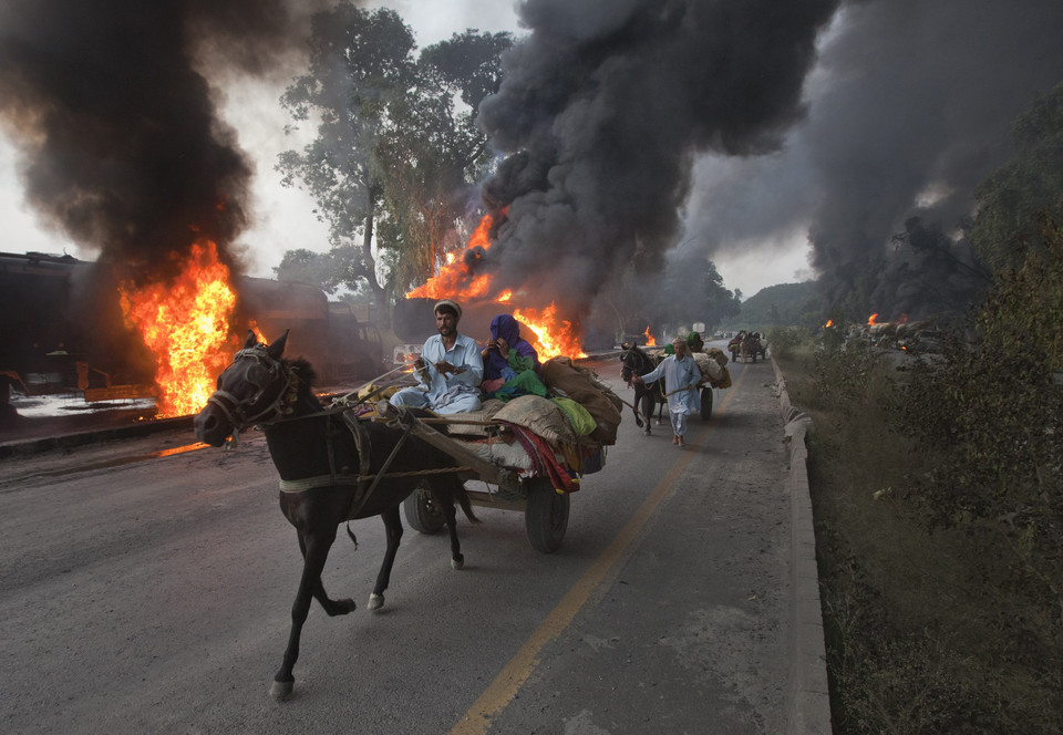 Residents on horse-led carts hurry past burning fuel tankers along the GT Road near Nowshera