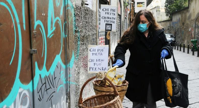 A woman puts food in a solidarity basket displayed with a note reading, Who can put, who cannot take in Naples, as Italy sees evidence it may have made it through the worst of the coronavirus pandemic