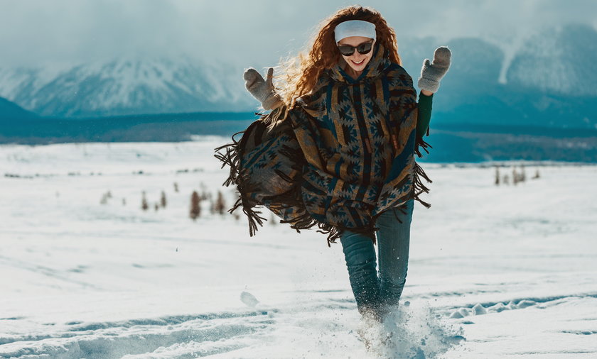 Happy young girl dressed in poncho runs in snow