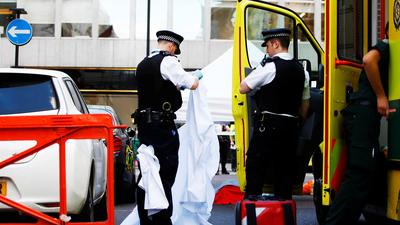Police officers unfold a sheet infront of a body covered with a blanket after the London Ambulance Service reported that a man collapsed and died from a heart attack in the Mayfair district of central London