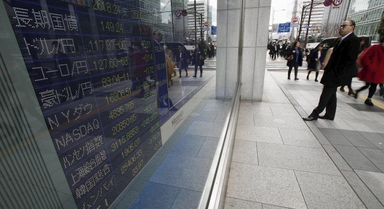 A pedestrian looks at an electronic board showing the exchange rates between (2nd top L to 4th) the Japanese yen against the U.S. dollar, the euro, and Australian dollar, and other market indices including Dow Jones and NASDAQ outside a brokerage in Tokyo, Japan, January 7, 2016.    REUTERS/Yuya Shino