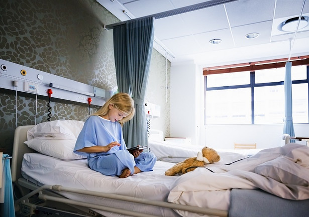 Little girl sitting on a hospital bed playing with a digital tablet