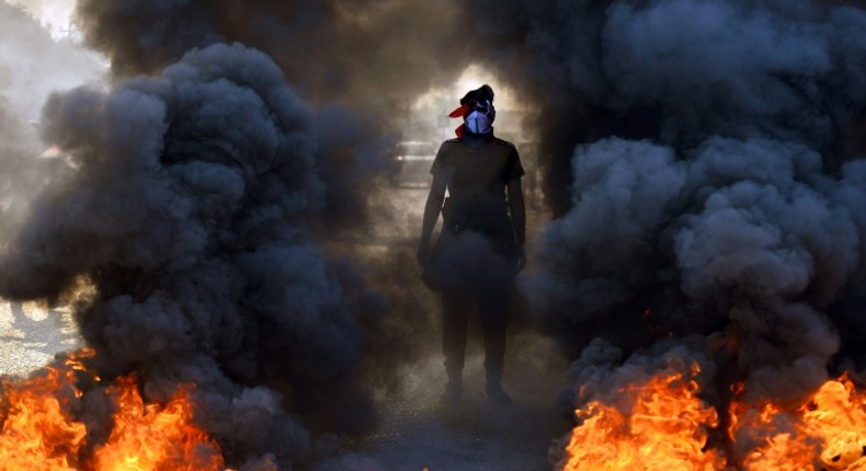 An Iraqi protester stands before burning tires at a roadblock in the central holy shrine city of Najaf