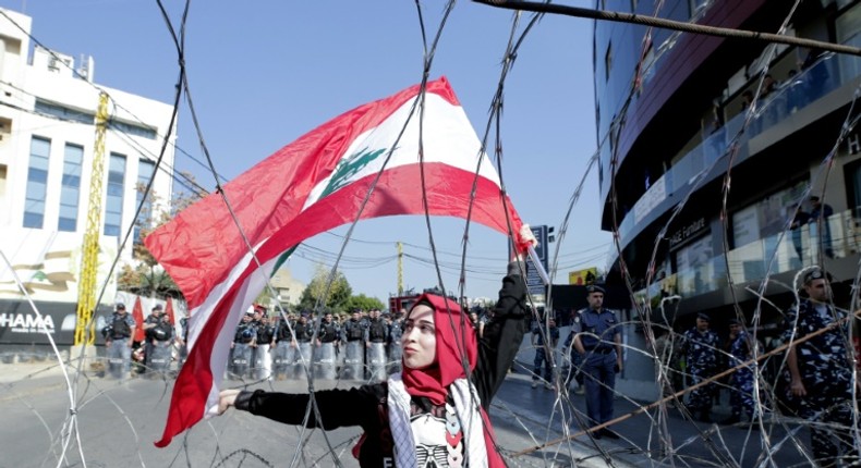 A Lebanese demonstrator waves the national flag while security forces stand by