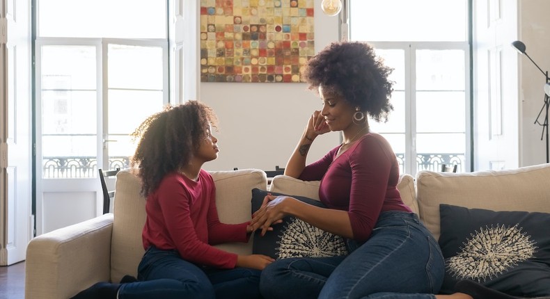 A woman holding hands with her daughter while sitting on couch [Photo: Kampus Production]