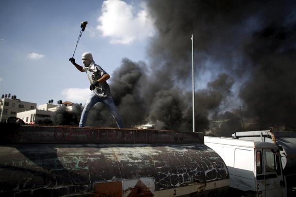 Palestinian protester uses a sling to hurl stones towards Israeli troops during clashes near the Jew