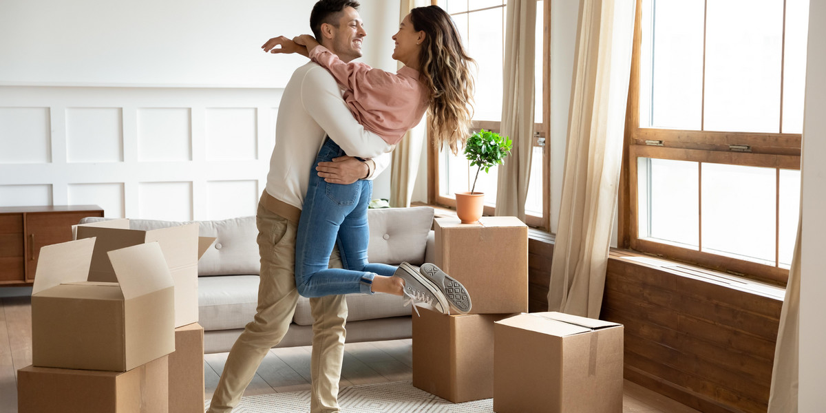 Happy husband lifting excited wife celebrating moving day with boxes