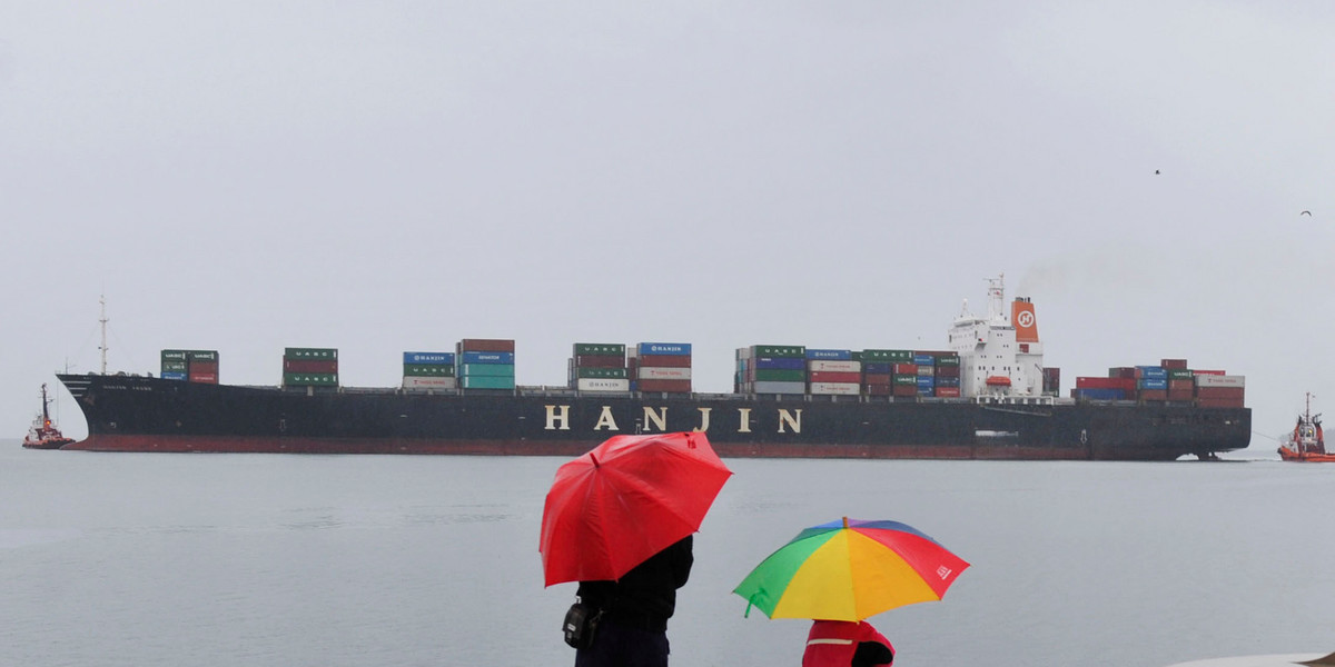 A father and son watch a South Korean Hanjin container ship pass.