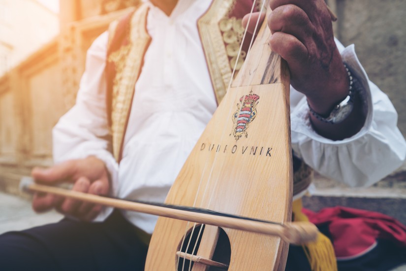 Busker gra tradycyjną chorwacką muzykę ludową na tradycyjnym 3-strunowym instrumencie, Dubrownik