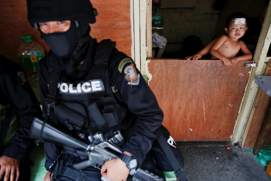 A baby looks at an armed member of a police SWAT team during a drug raid, in Manila, Philippines, October 7, 2016.
