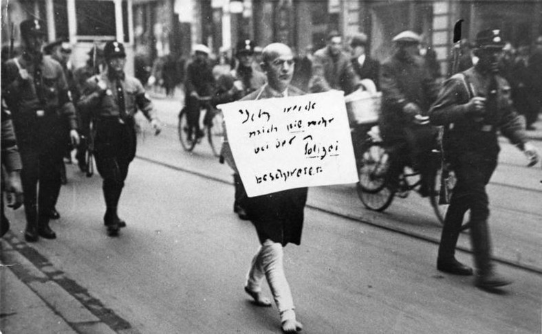 Naziści prowadzą żydowskiego prawnika ulicami Berlina. Mężczyzna idzie boso, na piersi ma napis: "Nigdy nie będę już narzekać na policję"
