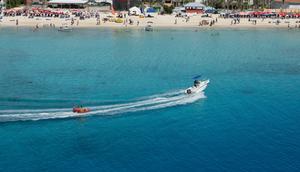 Motorboat pulling an inflatable seat over the turquoise waters of the Caribbean Sea in front of a busy beach. Grand Turk Island, Turks and Caicos Islands.Margaret Whittaker/Design Pics Editorial/Universal Images Group via Getty Images