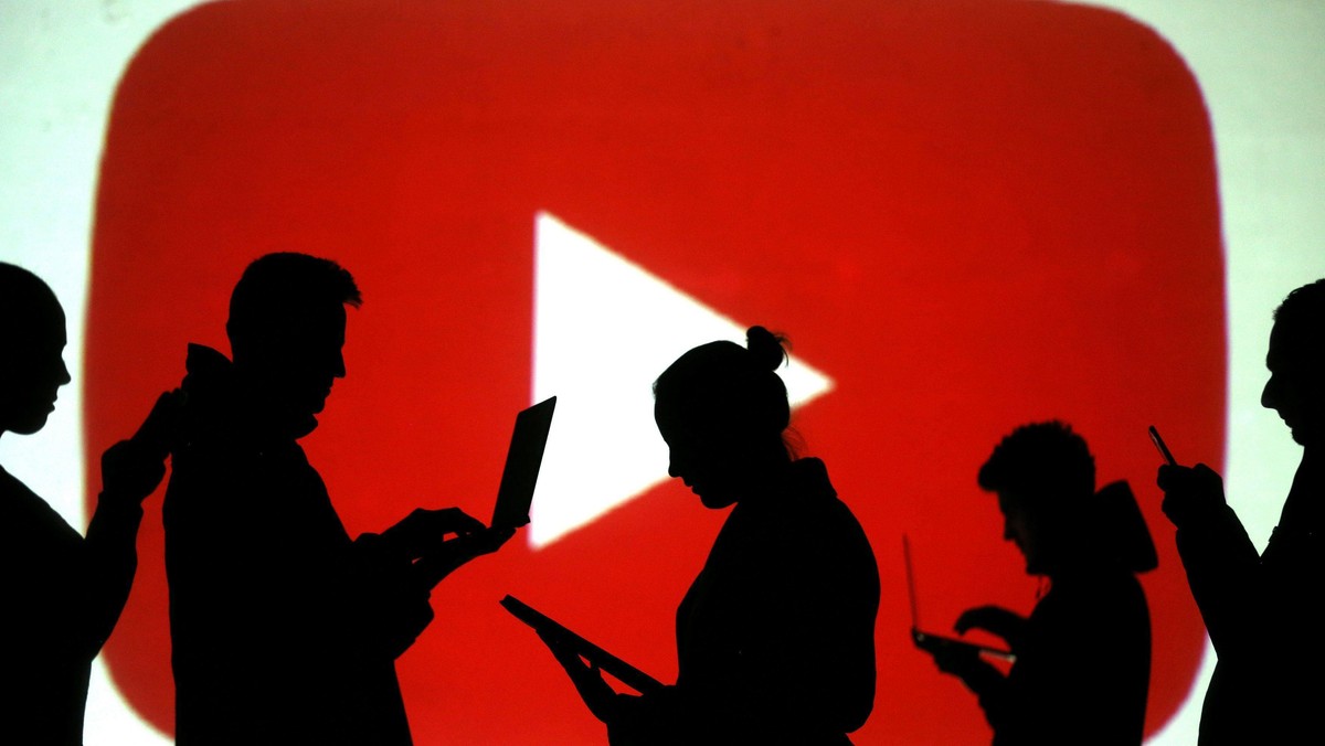 Silhouettes of laptop and mobile device users are seen next to a screen projection of Youtube logo i