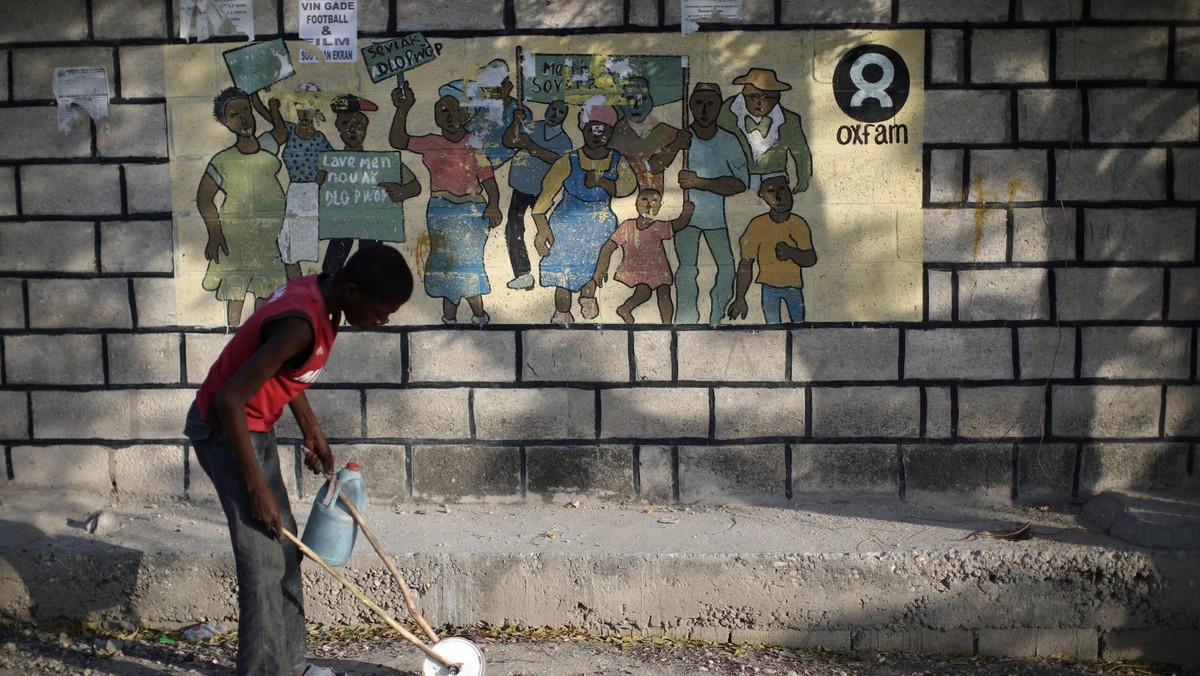 A boy playing with a homemade toy walks past an Oxfam sign in Corail, a camp for displaced people of