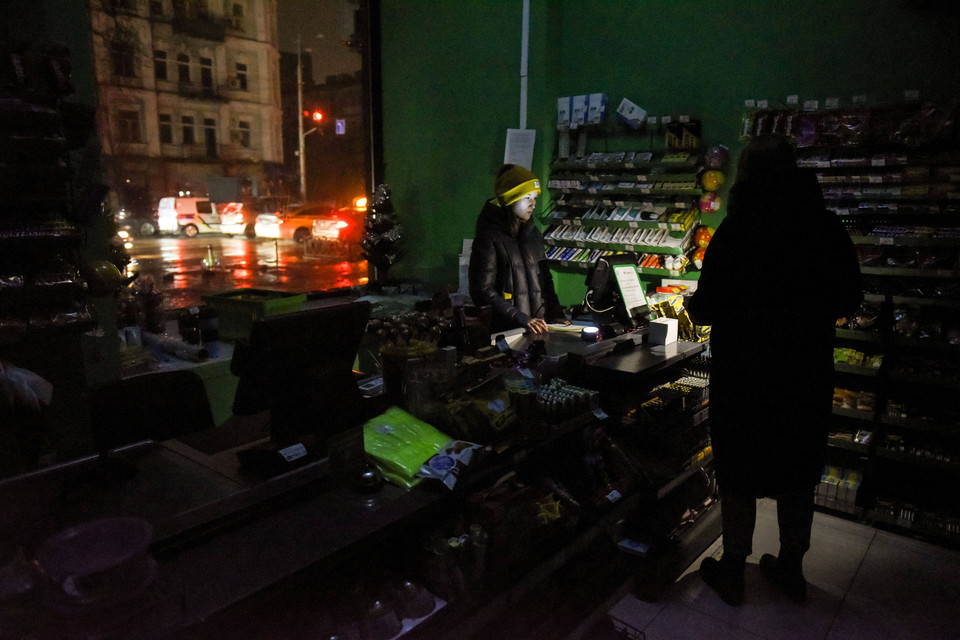 Sprzedawcy używają swoich telefonów, aby mieć światło w sklepie, podczas gdy prąd został wyłączony w Kijowie. 29.11.2022 r.