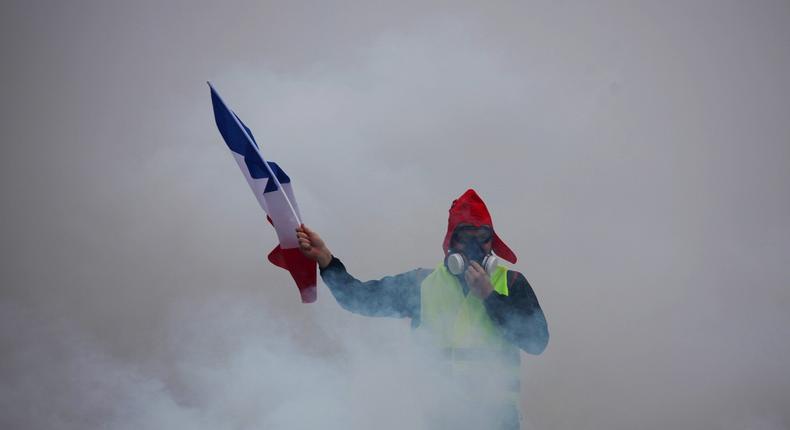 A demonstrator holds a French flag as he walks amid the tear gas during a protest of Yellow vests (Gilets jaunes) against rising oil prices and living costs, on December 1, 2018 in Paris. - Anti-government protesters torched dozens of cars and set fire to storefronts during daylong clashes with riot police across central Paris on December 1, as thousands took part in fresh 'yellow vest' protests against high fuel taxes.