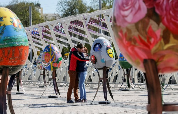 Couple kisses near traditional Ukrainian Easter eggs Pysanky, displayed at square, as part of upco