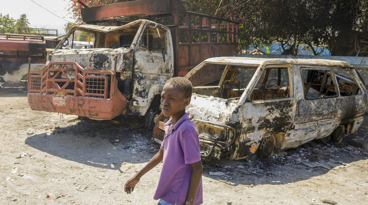 Kiégett rendőrségi járművek mellett megy el egy fiú egy bűnbanda által felgyújtott rendőrőrsnél a haiti fővárosban, Port-au-Prince-ban 2024. március 5-én/Fotó: MTI/AP/Odelyn Joseph