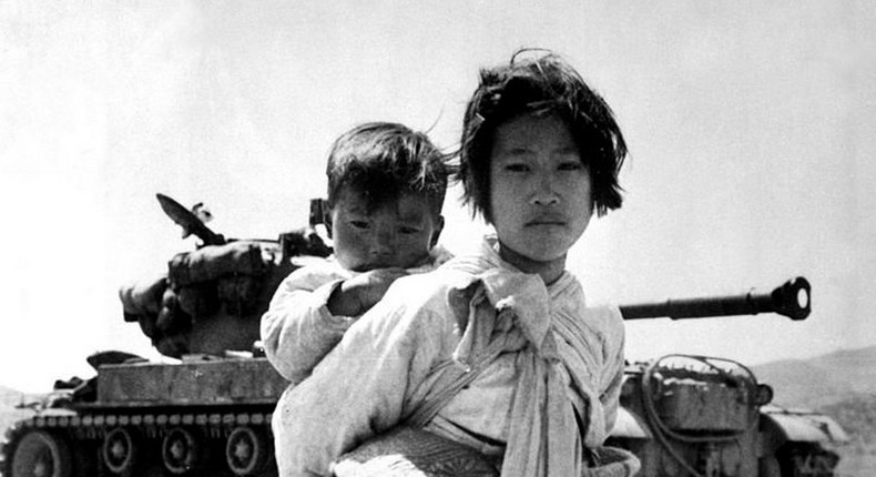 A mother and child in front of a tank during the Korean War.