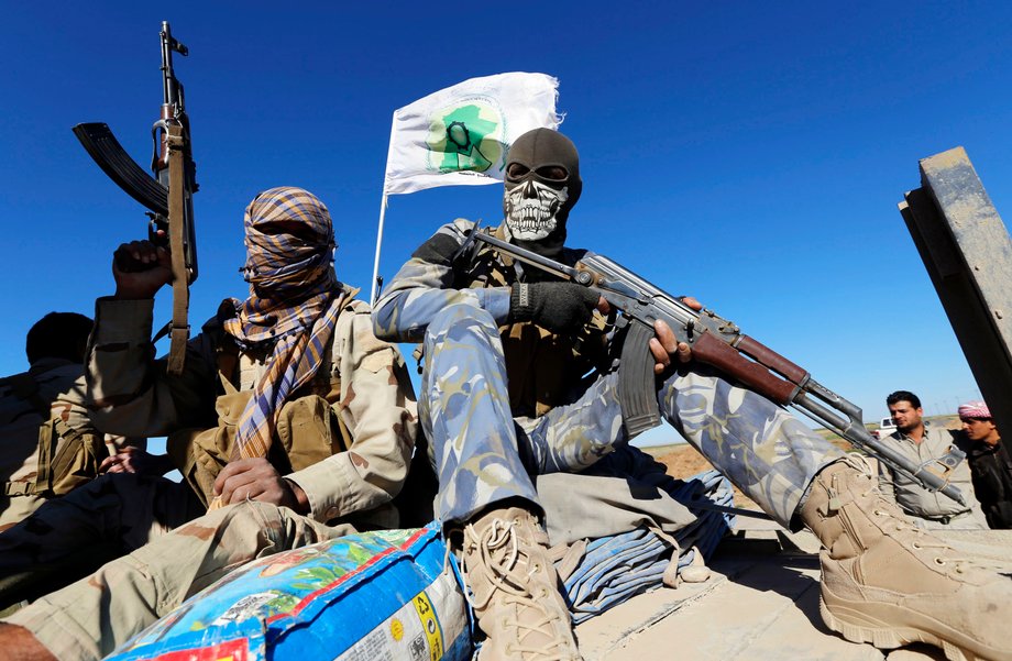 Masked Shi'ite fighters hold their weapons in Al Hadidiya, south of Tikrit, en route to the Islamic State-controlled al-Alam town, where they are preparing to launch an offensive on Saturday, March 6, 2015.