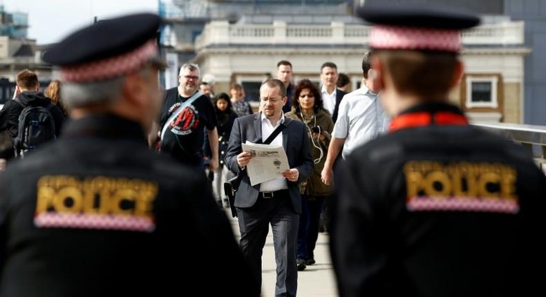 Police officers stand on duty as commuters walk across London Bridge in London on June 5, 2017, after it was partially re-opened following the June 3 terror attack