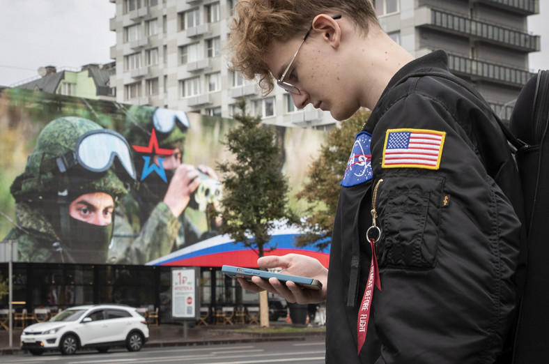 Putin kreuje wsparcie, którego mają udzielać mu młodzi ludzie. Na zdjęciu Rosjanin z naszytą flagą USA, w tle billboard reklamujący pobór do wojska, Moskwa, Rosja, 18 września 2023 r.