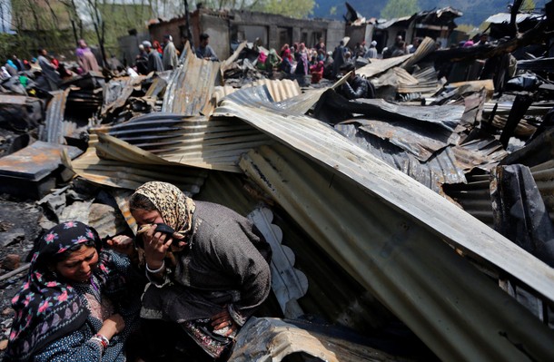 Women weep as they sit around remains of their houses gutted in a fire which broke out in a resident