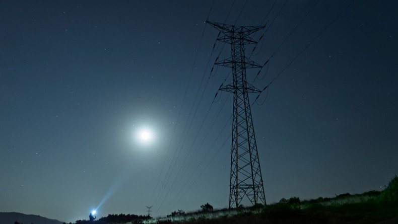 Power outage: A high-voltage tower on a mountain with an electrician carrying flashlights repairing a fault at night. [Stock Photo/Getty Images]