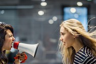 Profile view of angry female manager yelling at her colleague through megaphone.