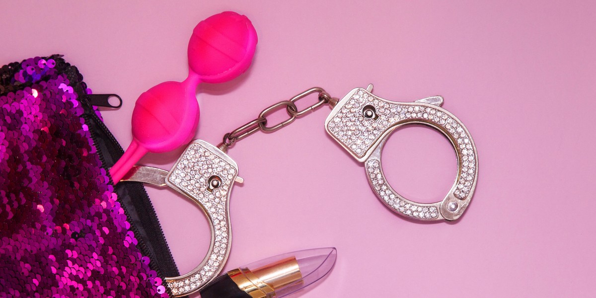 Different sex toys: sex balls, handcuffs and lipstick in a Bright violet female cosmetics bag from t