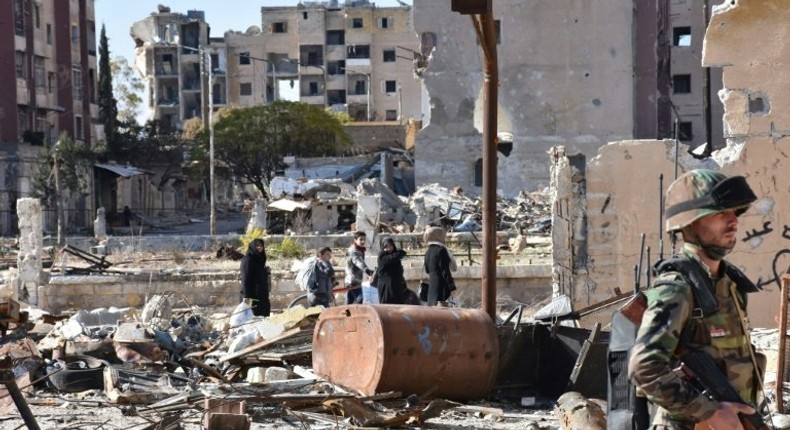 Syrians walk amid debris as a soldier secures the Masaken Hanano neighbourhood in Aleppo, on December 6, 2016