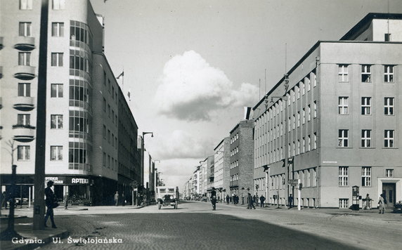Gdynia – ul. Świętojańska w 1938 r. Pierwsza ulica poza prowadzącymi do morza, która została wybrukowana i urządzona zgodnie z ówczesnym, nowym planem miasta. Intensywna zabudowa ulicy kamienicami nastąpiła po nadaniu Gdyni praw miejskich w 1926 r. Podczas okupacji Niemcy zmienili nazwę ulicy na Adolf Hitler Straße, przechodziła przez Sopot, a zaczynała się przy dworcu Gdańsk Główny