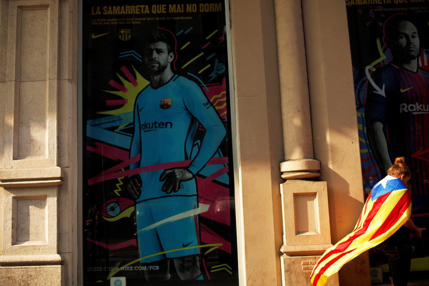 A woman wrapped in an Estelada stands next to an advertisement showing an image of Gerard Pique outs