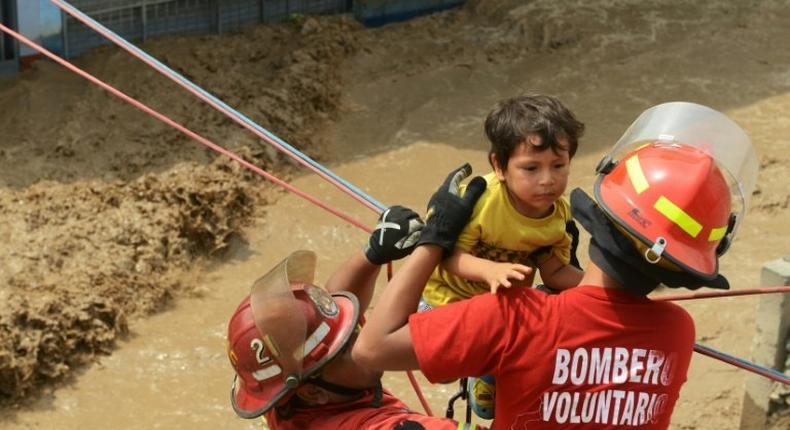 Residents of the Huachipa populous district, east of Lima, are helped on March 17, 2017, by police and firemen rescue teams to cross over flash floods hitting their neighbourhood and isolating its residents