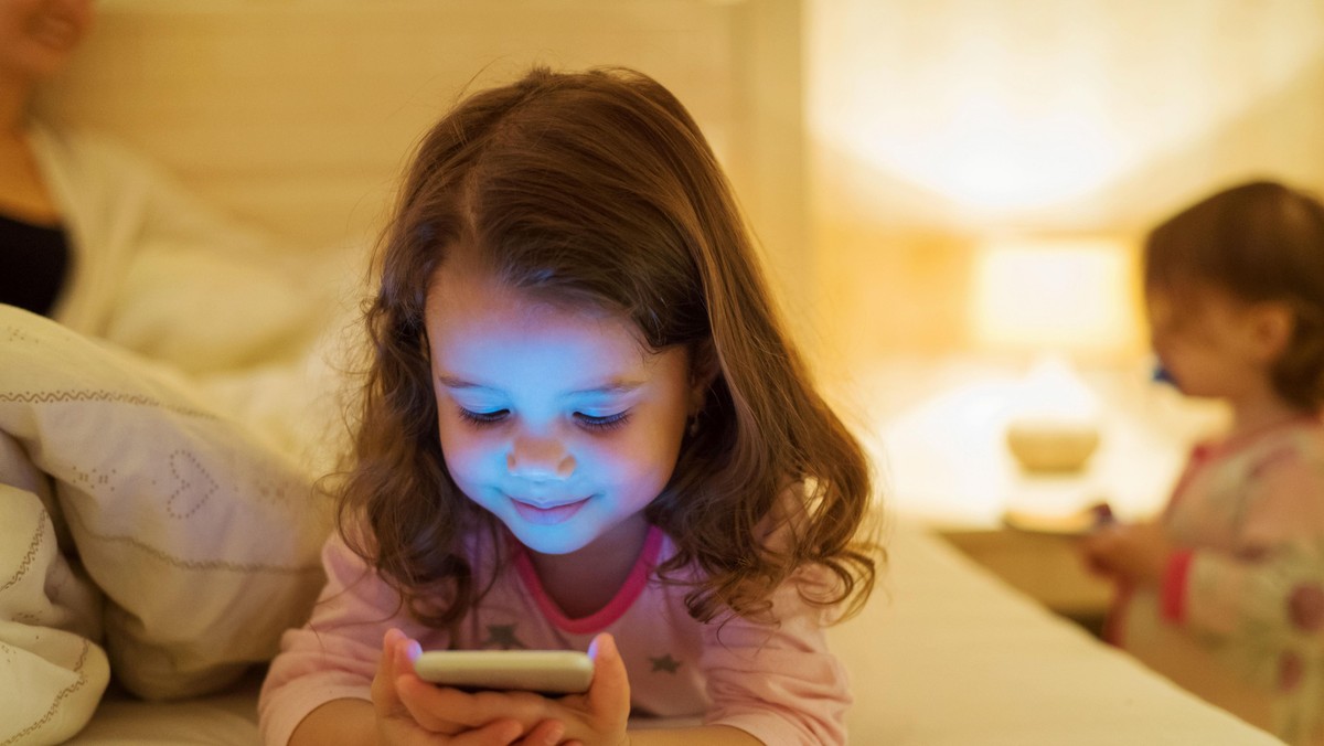 Little girl with smartphone lying in a bed, bedtime