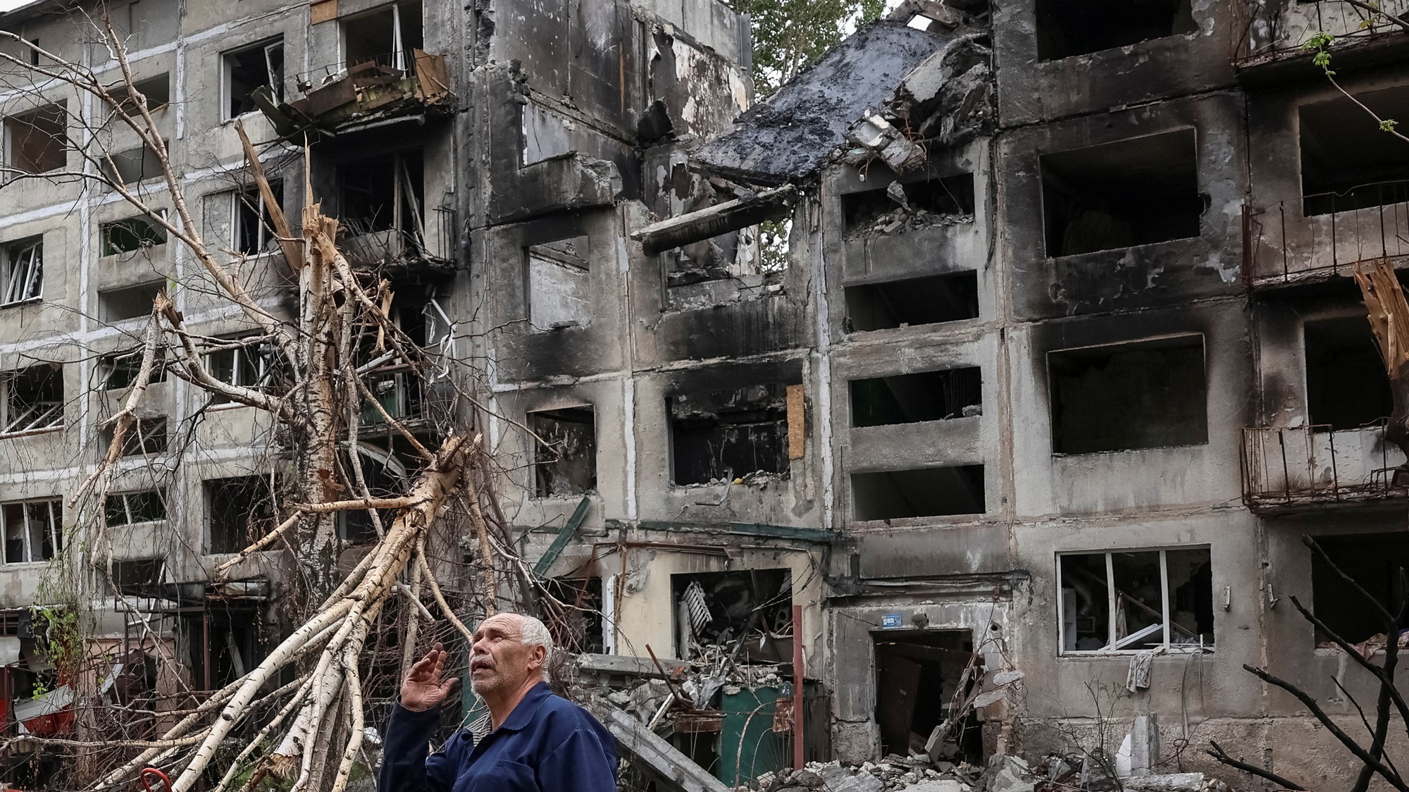 Obyvateľ stojí pri budovách poškodených ruskými vojenskými útokmi, REUTERS/Anatolii Stepanov