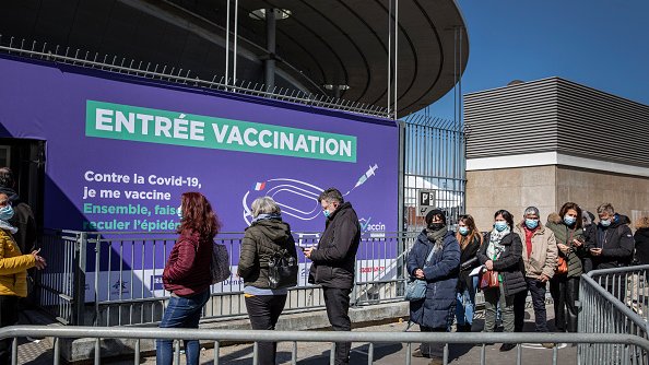 Ludzie stojący w kolejce przed paryskim Stade de France po przekształceniu go w centrum szczepień przeciw COVID-19