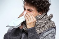 Ill young man with red nose, scarf and cap sneezing into handkerchief